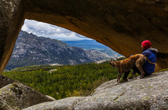 Person looking at the landscape with his dog in front of a rock bridge in the pedriza