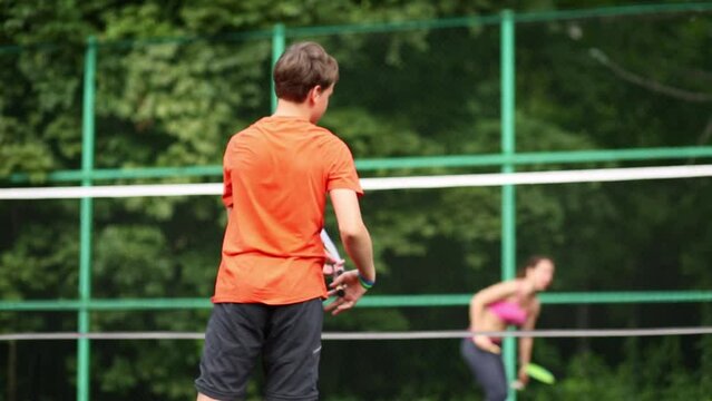 Boy playing badminton with his mother on the playground, rear view