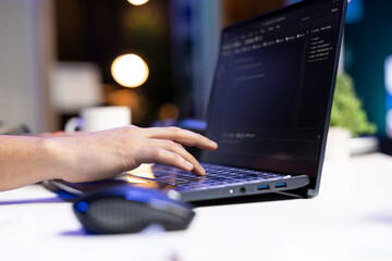 An individual is managing a system, typing on a keyboard while a laptop screen shows software programming. Person computing code, working on data center and network security.