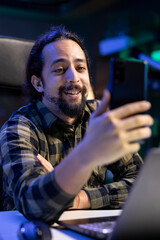 Closeup of happy male individual taking a selfie using his smartphone. Smiling bearded man grasping his mobile device and making a video for his social media accounts.