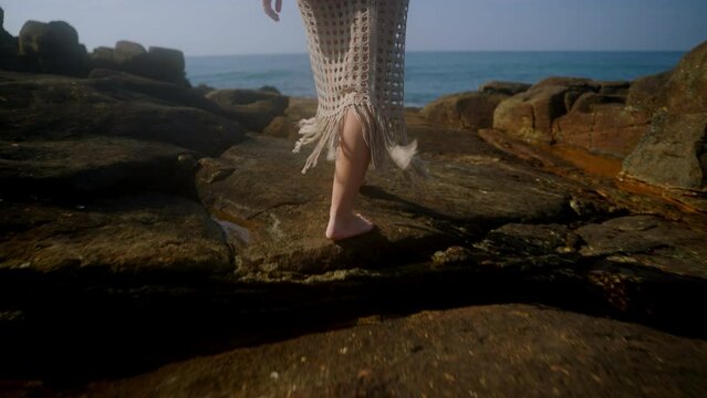 Woman in VR headset explores virtual world, gestures touch on rocky beach. Digital interaction, immersive experience in natural seascape setup. VR travel, futuristic leisure by ocean. Slow motion.