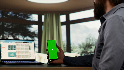 Adult millionaire looks at greenscreen smartphone display in his luxurious villa in the woods,...