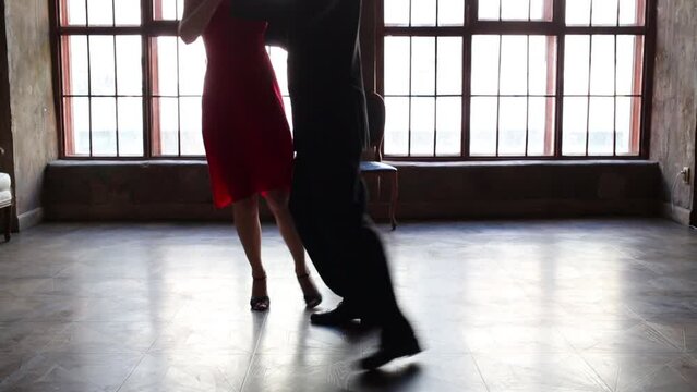 Legs of woman in red and man in black dancing tango near window