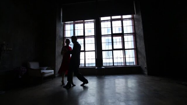 Girl in red dress and man in black suit dance tango