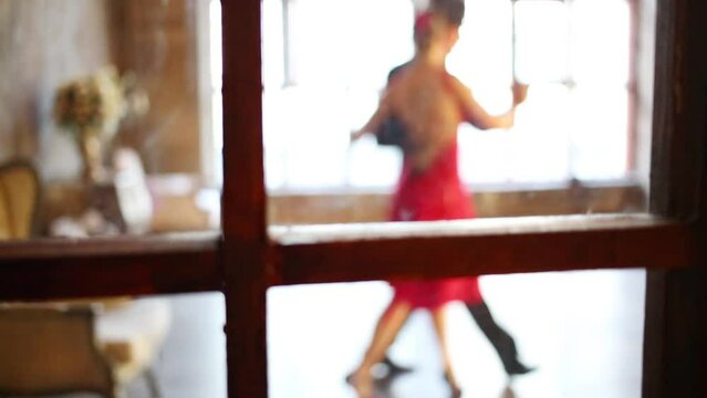 Young couple dance tango behind window out of focus