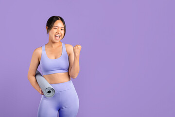 Young Asian woman in sportswear with fitness mat, gesturing yes on purple backdrop