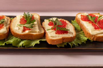 Sandwiches with red caviar. Black rectangular platter. On pink wooden tray