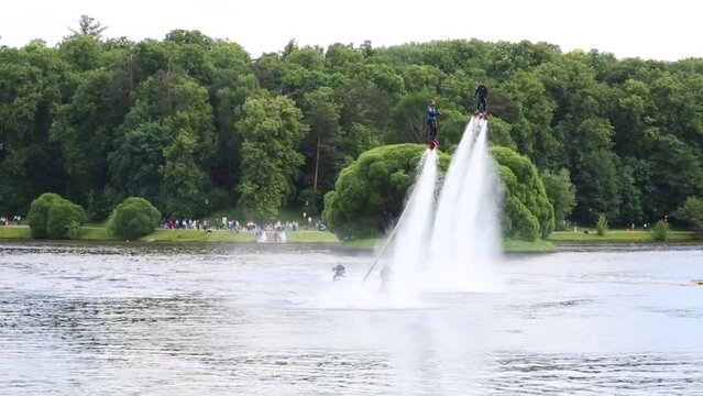 Athletes flyboard and accompanying them on jet skis on lake in park.