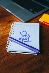 Photograph of notebook on a wooden table with hand drawn March 8 heart. Concept of people and lifestyles.