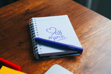 Photograph of notebook on a wooden table with hand drawn March 8 heart. Concept of people and lifestyles.