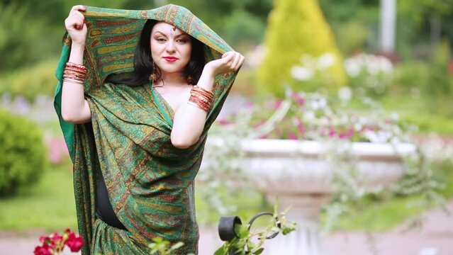 woman in sari dressing her on head and turning in front of flowerbeds