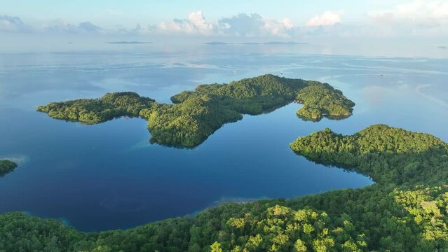Sunrise illuminates calm seas around the islands of Gam and Yangeffo in Raja Ampat, Indonesia. This tropical region is mostly known for its exquisite coral reefs and overall high marine biodiversity.