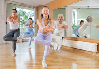 Group of smiling women of different ages dancing and practicing new movements in class. Sport,...