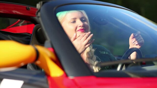 Blonde woman in red sport car looks in mirror and keeps wheel