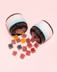 Two jars of fruit gummies spilling out on pink background