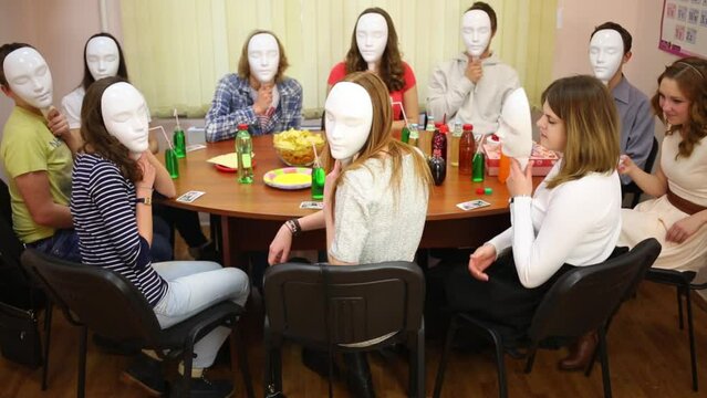 Ten young people hides faces by masks at table in room