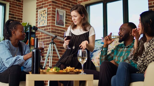 Caucasian woman having interesting discussion with multiethnic apartment party guests, sharing enthralling story with them. Host talking with friends in stylish living room