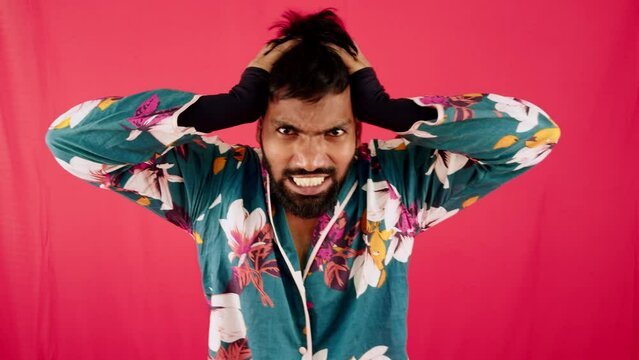 Angry young man with hands on head against a red background wearing a floral shirt expressing frustration