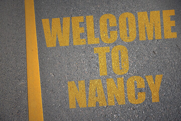 asphalt road with text welcome to Nancy near yellow line.