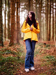 Young teenager girl in yellow jacket on a path in dense forest