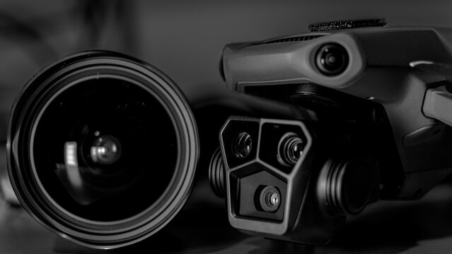 Black and white macro image with the front right angle of a drone with 3 camera gimbal, and a wide angle camera lens.