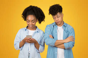 A smiling young woman is engrossed in her smartphone while a young man