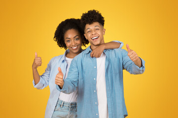 Two joyful young adults give enthusiastic thumbs up to the camera, showcasing positivity and...