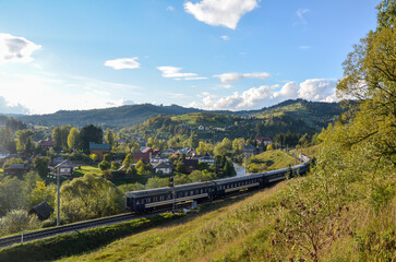 Naklejka premium Beautiful mountain landscape with a train on railway passing by a picturesque Vorokhta village on a sunny autumn day. Carpathian Mountains, Ukraine