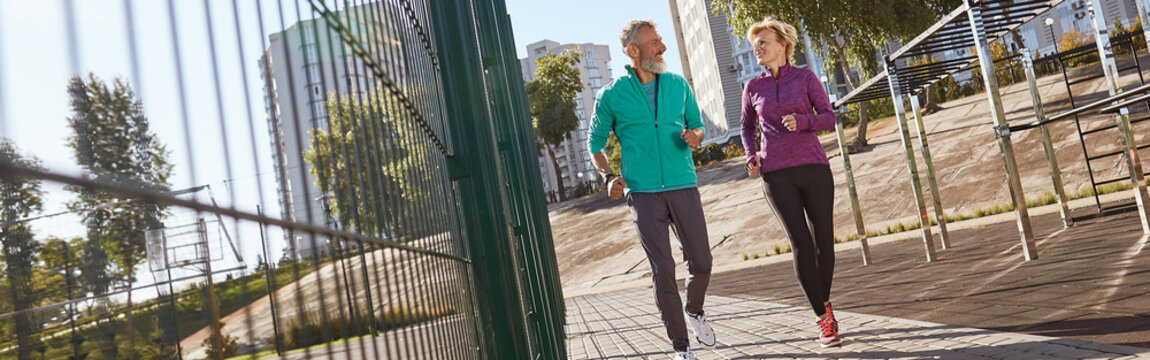 Morning jog. Active mature family couple in sportswear running together at the stadium in the early morning. Full length. Beautiful seniour couple doing sport outdoors