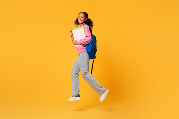 Fototapeta na wymiar Happy black student girl jumping with backpack and workbooks, studio