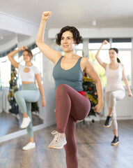 Cheerful active young adult Latina in colorful sportswear enjoying modern vigorous dance at group...