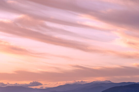 A beautiful serene lilac sunset overlooking layers of hills and mountains, sweeping clouds and soft warm light. A picture that is quite meditative and peaceful that could be used to promote wellbeing
