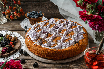 Delicious biscuit cake with cream and berries on wooden rustic background with cup of tea, flowers, lace napkins. Sweets, dessert and pastry, homemade cakes, top view