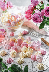 Pastel coloured meringues, zephyr, on lace napkin with cup of tea and rose flowers on light background. Sweets, dessert and pastry, homemade cakes, top view, selective focus