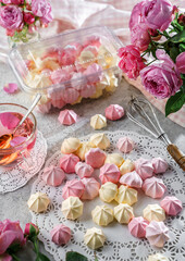 Pastel coloured meringues, zephyr, on lace napkin with cup of tea and rose flowers on light background. Sweets, dessert and pastry, homemade cakes, top view