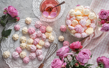 Fototapeta na wymiar Pastel coloured meringues, zephyr, on lace napkin with cup of tea and rose flowers on light background. Sweets, dessert and pastry, homemade cakes, top view