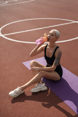 Active woman takes a hydrating break during her workout, sitting on a purple yoga mat outdoors