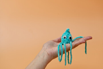 A women's hand holding a Crochet blue octopus toy, on an orange background, advertising or presentation concept © Höyka Studio
