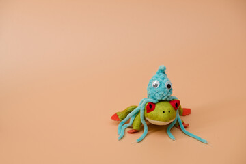 Crochet blue octopus toy sitting on a plush frog, orange background, advertising or presentation concept