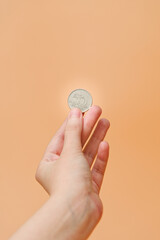 A women's hand holding a Hungarian forint coin, on an orange background