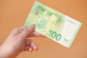 A woman's hand holds 100 euro cash currency, on an orange background.