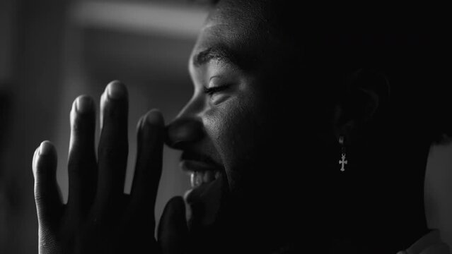 One happy young black man PRAYING in feeling HOPEFUL. Faithful African American person profile close-up face smiling in black and white, monochromatic