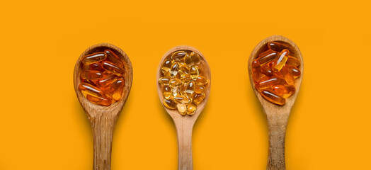 Spoons with fish oil capsules on orange background, top view