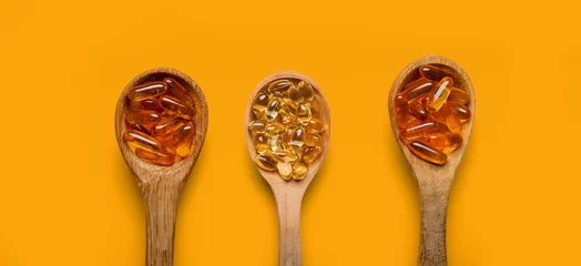 Schilderijen op glas Spoons with fish oil capsules on orange background, top view © Pixel-Shot