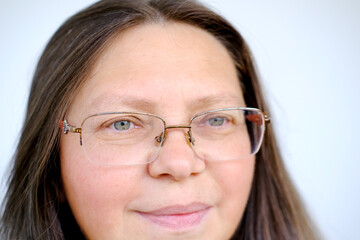 close-up female face of elderly woman 50 years old with long hair in glasses, on lips slight smile of maturity, inner strength resilience, mature appearance and graceful wisdom, knowledge, experiences