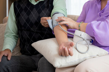 Closeup hands asian senior couple sitting on sofa checking blood pressure with pressure gauge in living room at home, elderly man and woman checkup health and pressure, medical of patient.