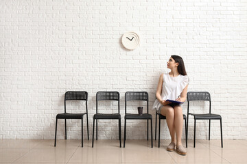 Young woman looking at clock while waiting for job interview in room