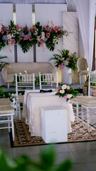 Place for wedding ceremony in white color ,with white fireplace and chandeliers decorated with flowers and white cloth and wooden chairs for guests on each side outdoors.