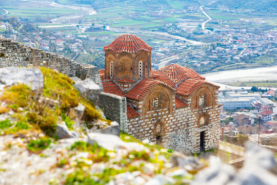 View of Byzantine style building of medieval Holy Trinity Church on green flowering slope of hill in Berat in rays of spring sun, Albania