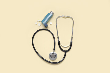 Stethoscope with asthma inhaler and pills on yellow background